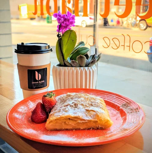 A flaky pastry with strawberries on an orange plate beside a coffee