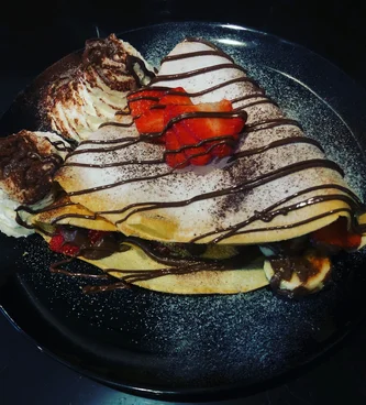 A crepe topped with chocolate drizzle and strawberries on a dark plate