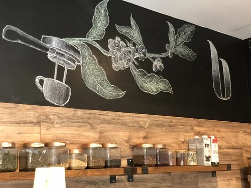 A chalkboard drawing of a coffee plant and espresso machine above shelves of jars