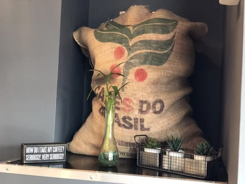 A burlap coffee sack printed Café do Brasil with a plant in a glass vase