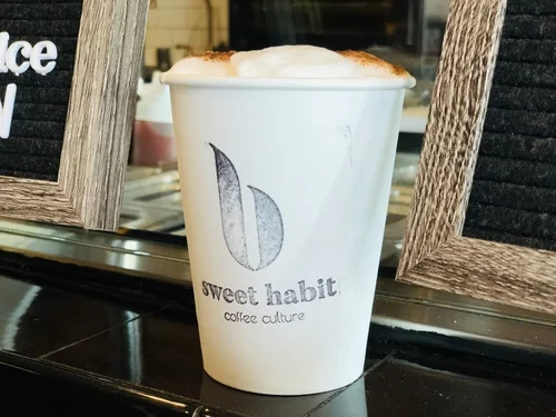 A white Sweet Habit cup topped with foam on the counter