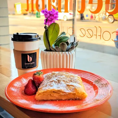 A flaky pastry with strawberries on an orange plate beside a coffee