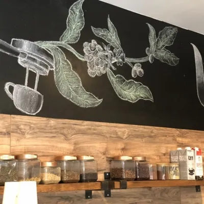 A chalkboard drawing of a coffee plant and espresso machine above shelves of jars