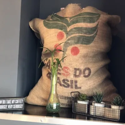 A burlap coffee sack printed Café do Brasil with a plant in a glass vase